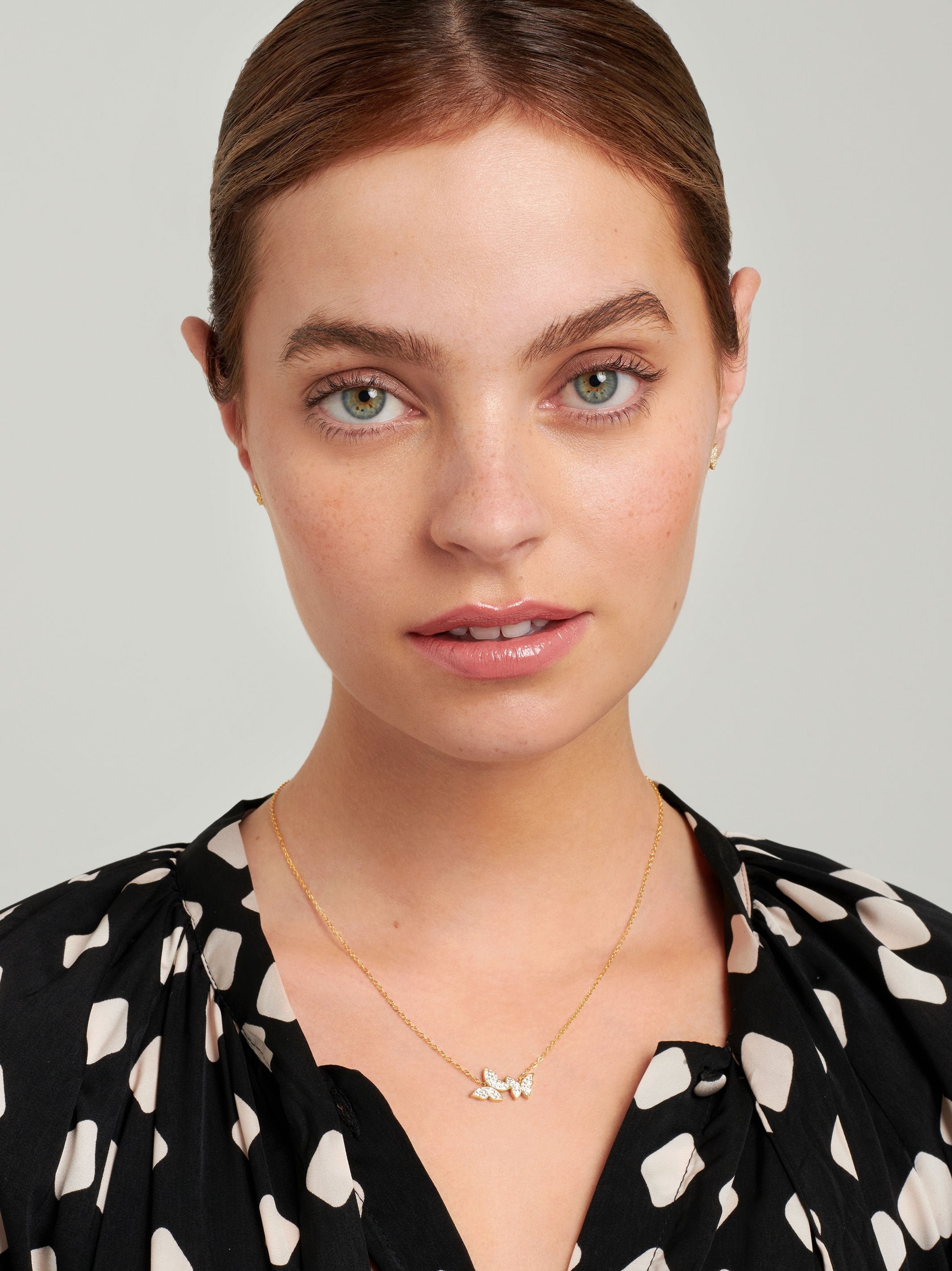 Teenage model wearing a gold necklace with two butterflies.