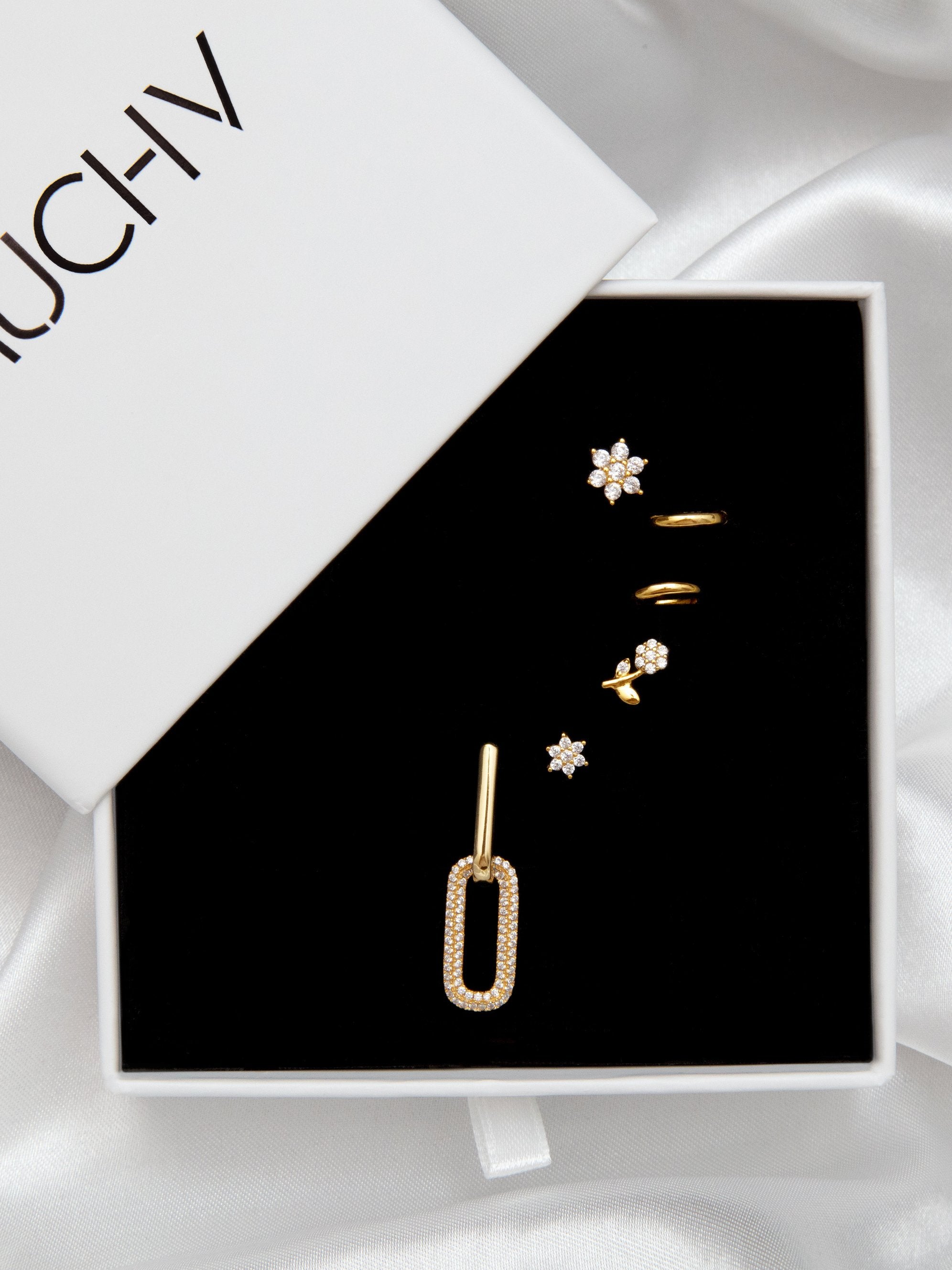 Flower stud earrings styled with various gold earrings inside a gift box.