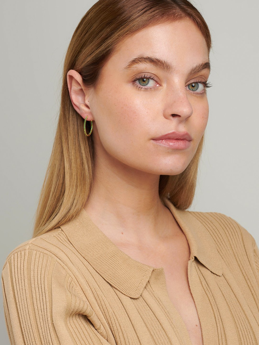 Emerald green hoop earrings in gold with stones on the inside and outside.