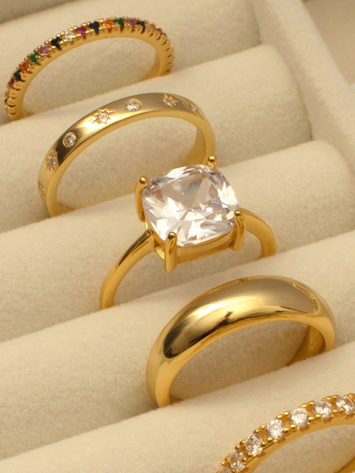 Gold ring with a square stone, next to various other rings.