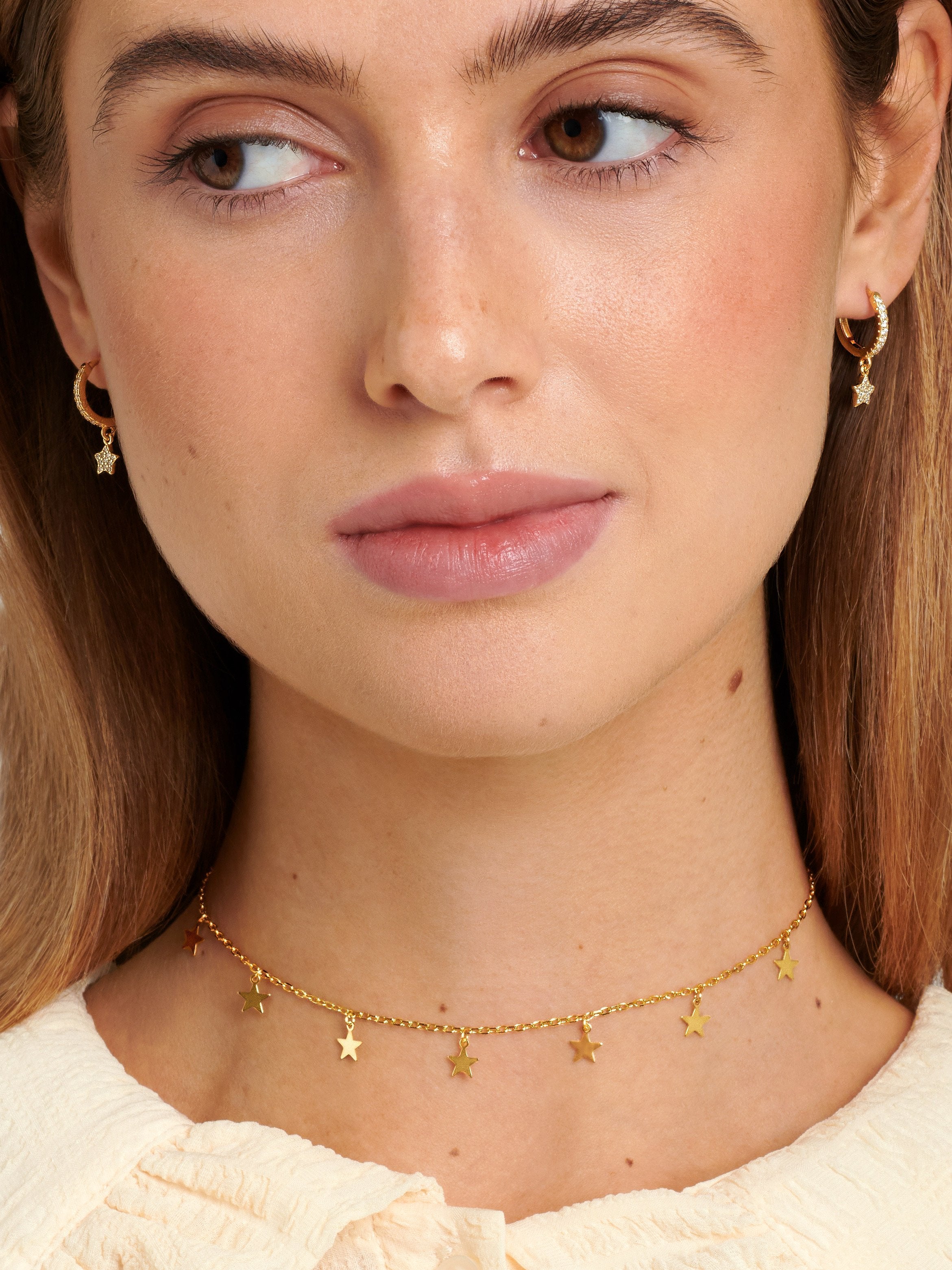 Model wearing a gold star choker paired with star charm hoop earrings.