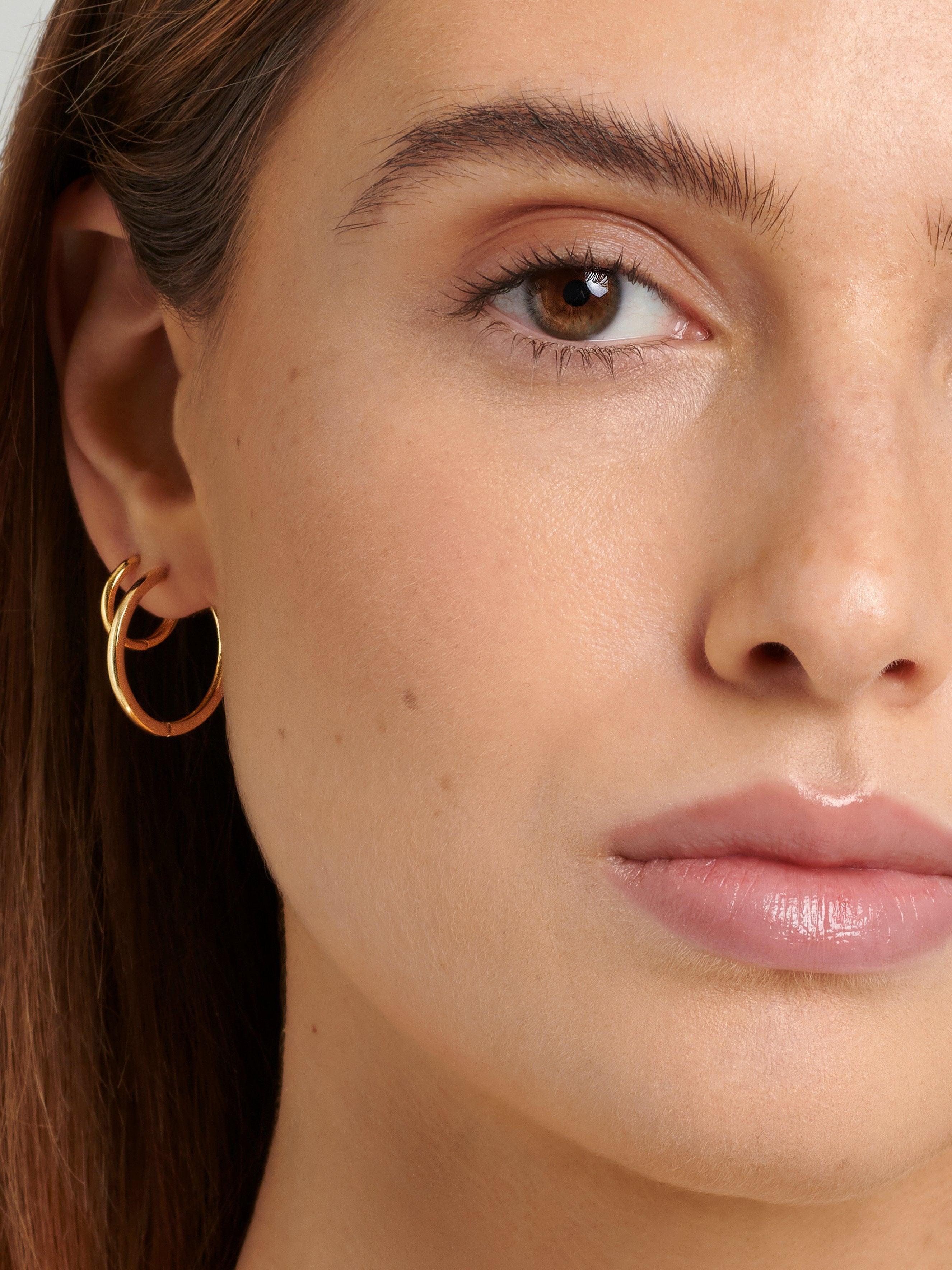 Female model wearing thin Gold Hoop Earrings in her lobe piercing.