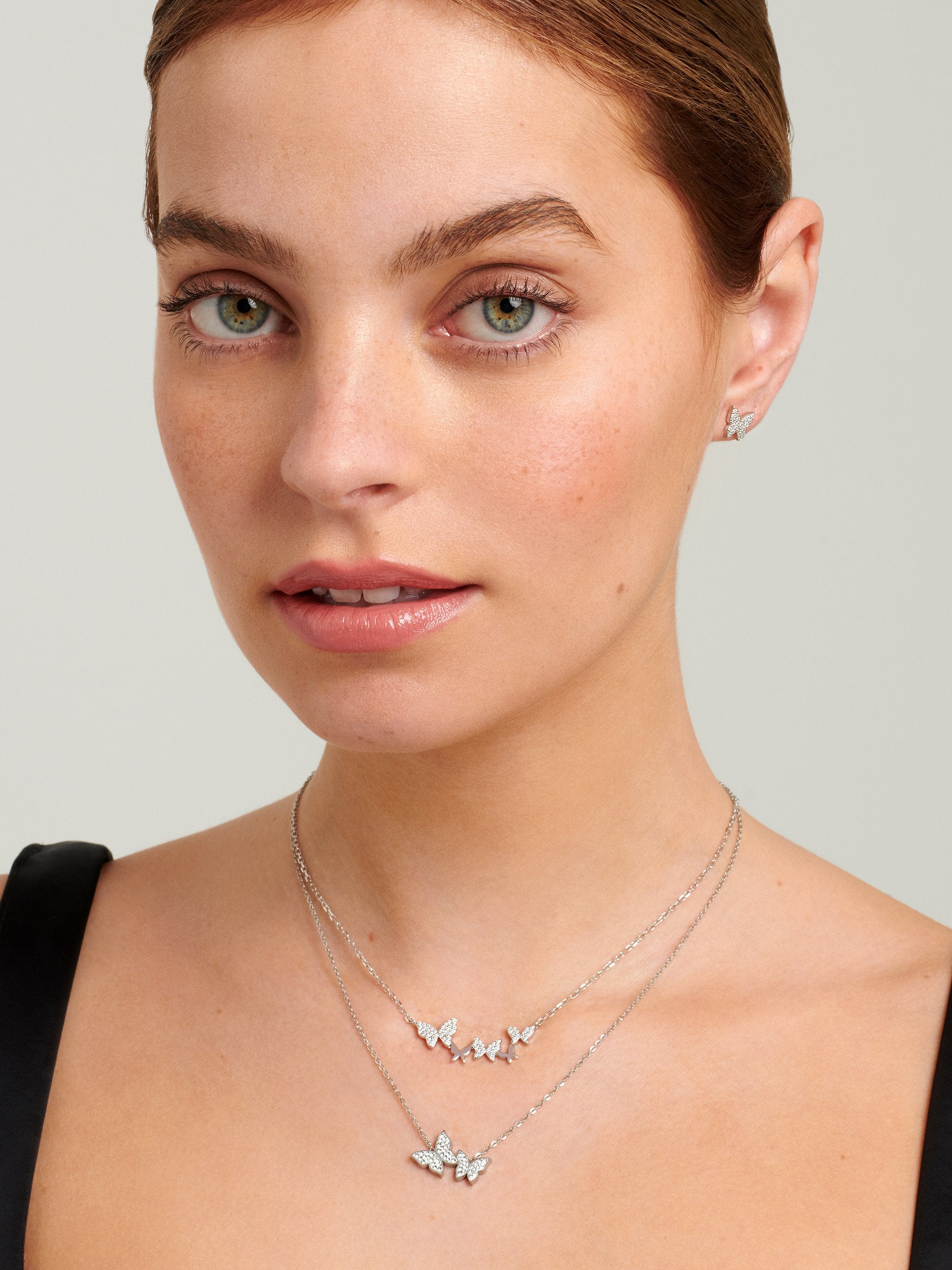Female model wearing two different butterfly necklaces in silver layered together.
