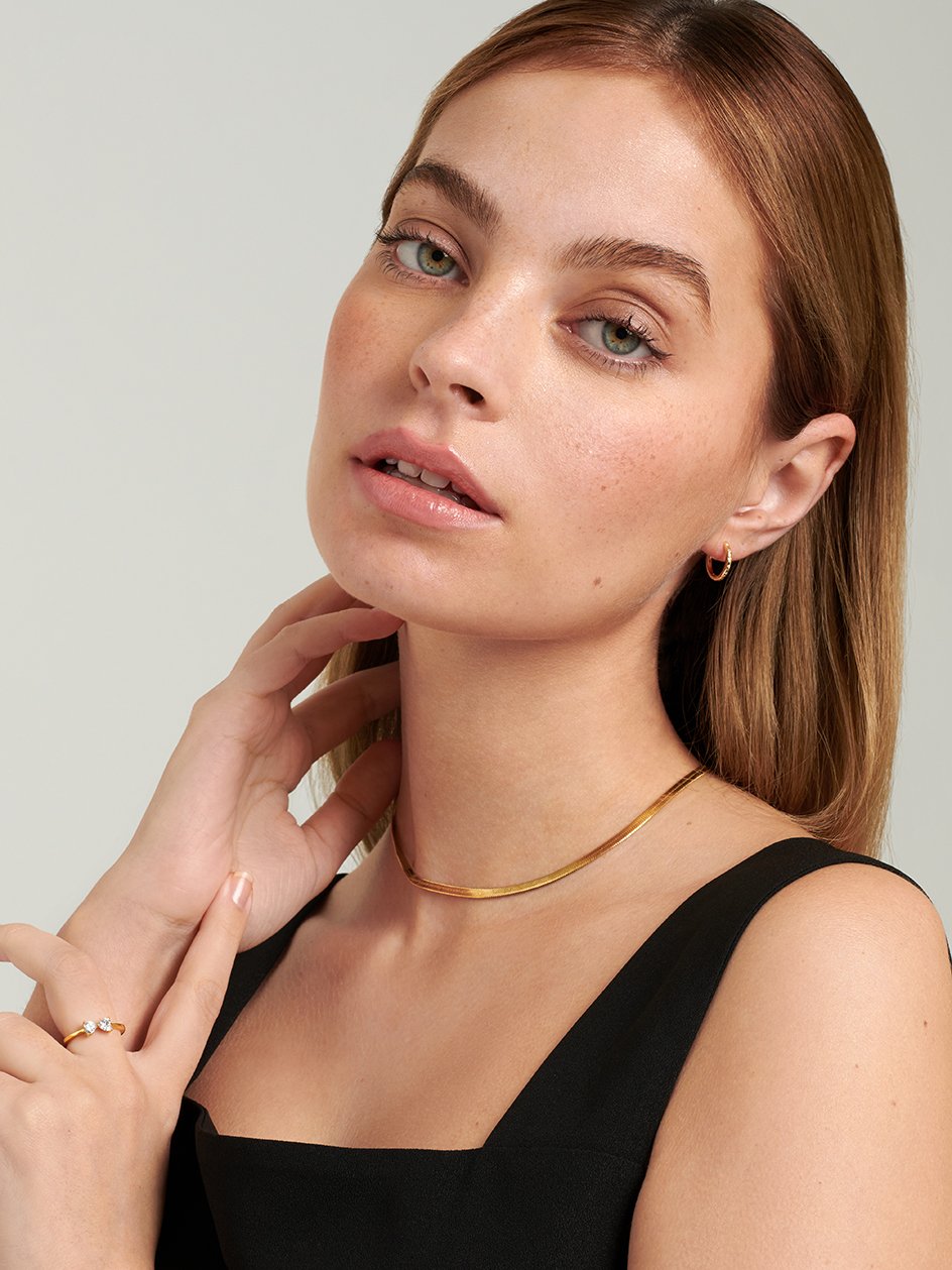 Female model wearing gold Herringbone Necklace paired with simple gold hoop earrings.