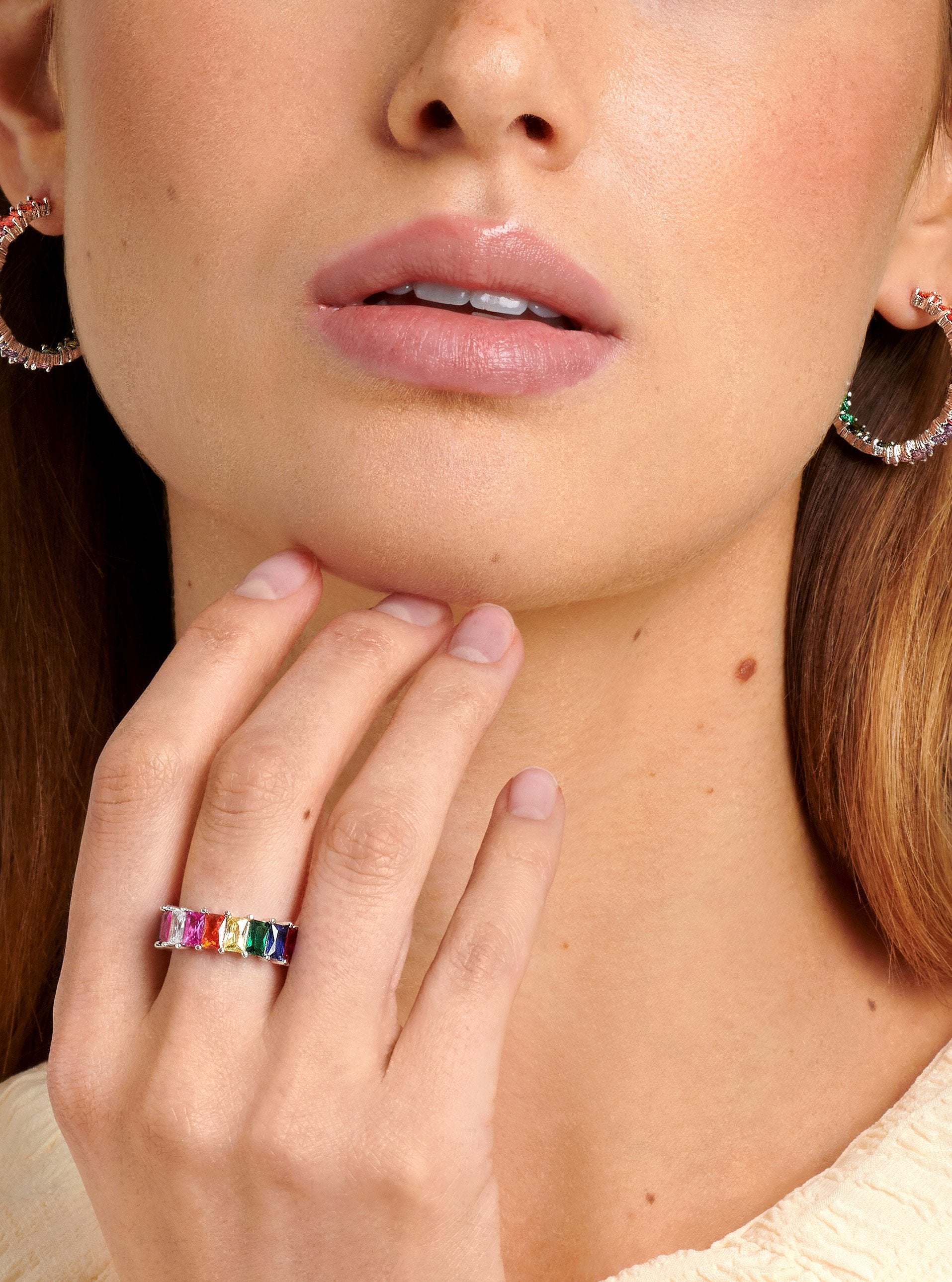Model wearing a silver ring with colourful rainbow stones - paired with big hoop earrings.