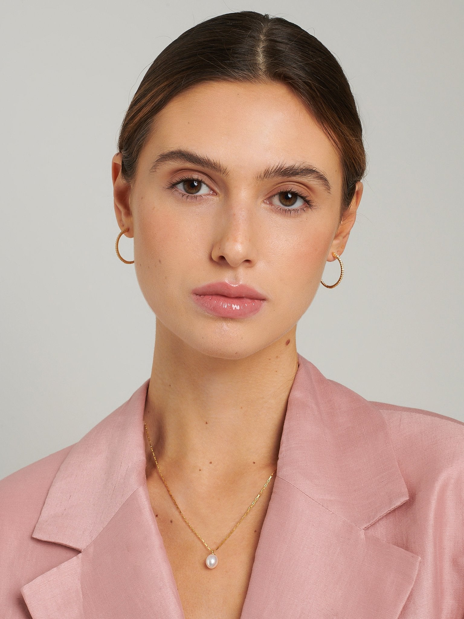 Female model wearing a pink blazer with a gold pendant necklace.