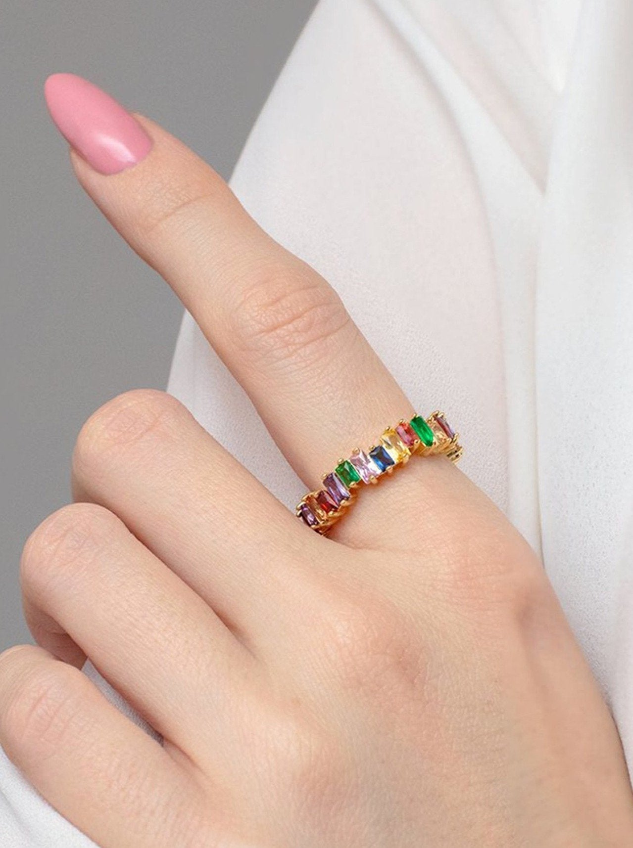 Model with pink nails wearing a colourful rainbow ring.