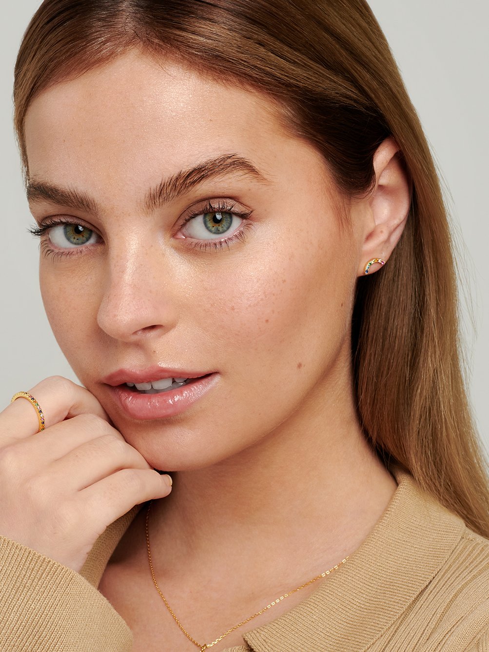 Female model wearing rainbow stud earrings in her earlobe piercing.