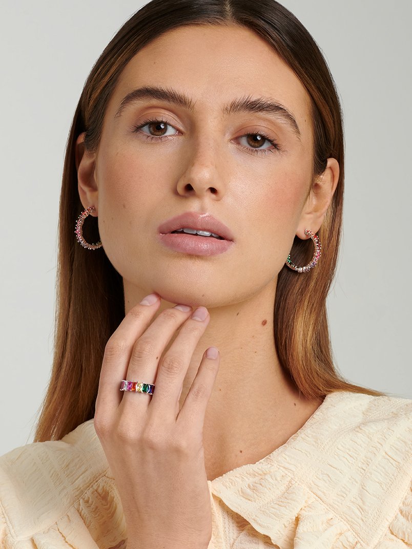 Model wearing large silver hoop earrings with colourful stones paired with a statement silver rainbow ring.