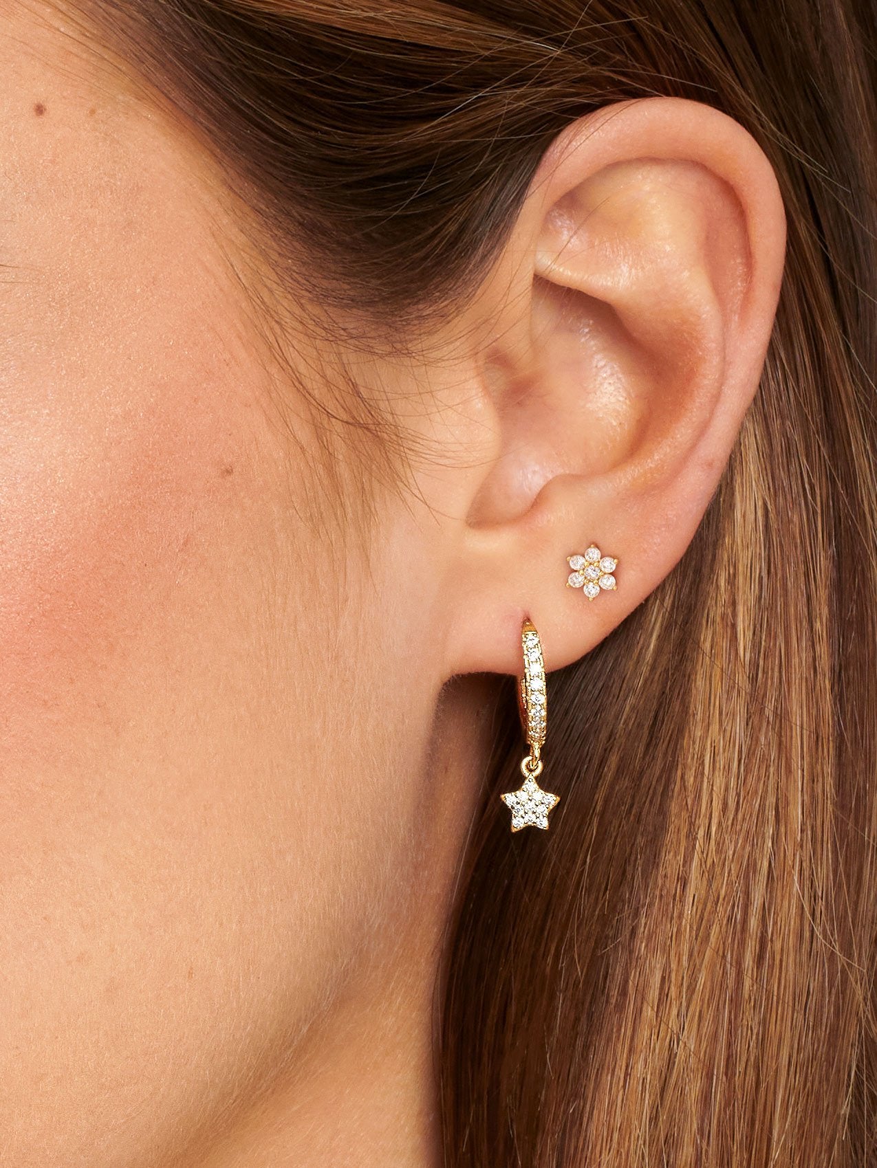 Tiny gold flower stud earrings paired with dangling star charm hoops.