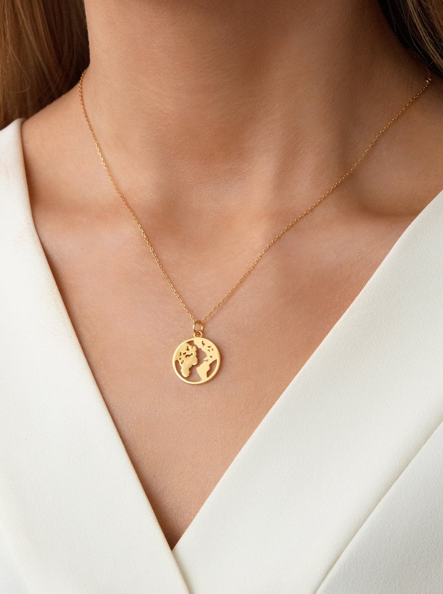 Female model wearing a gold necklace with small globe pendant.